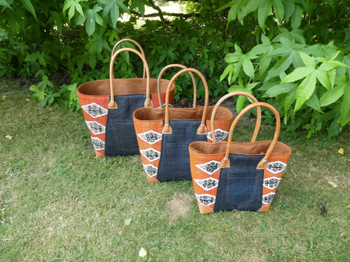 Cabas africain motif orange en cuir, panier artisanal trois tailles - photo de trois paniers tressés sur herbe