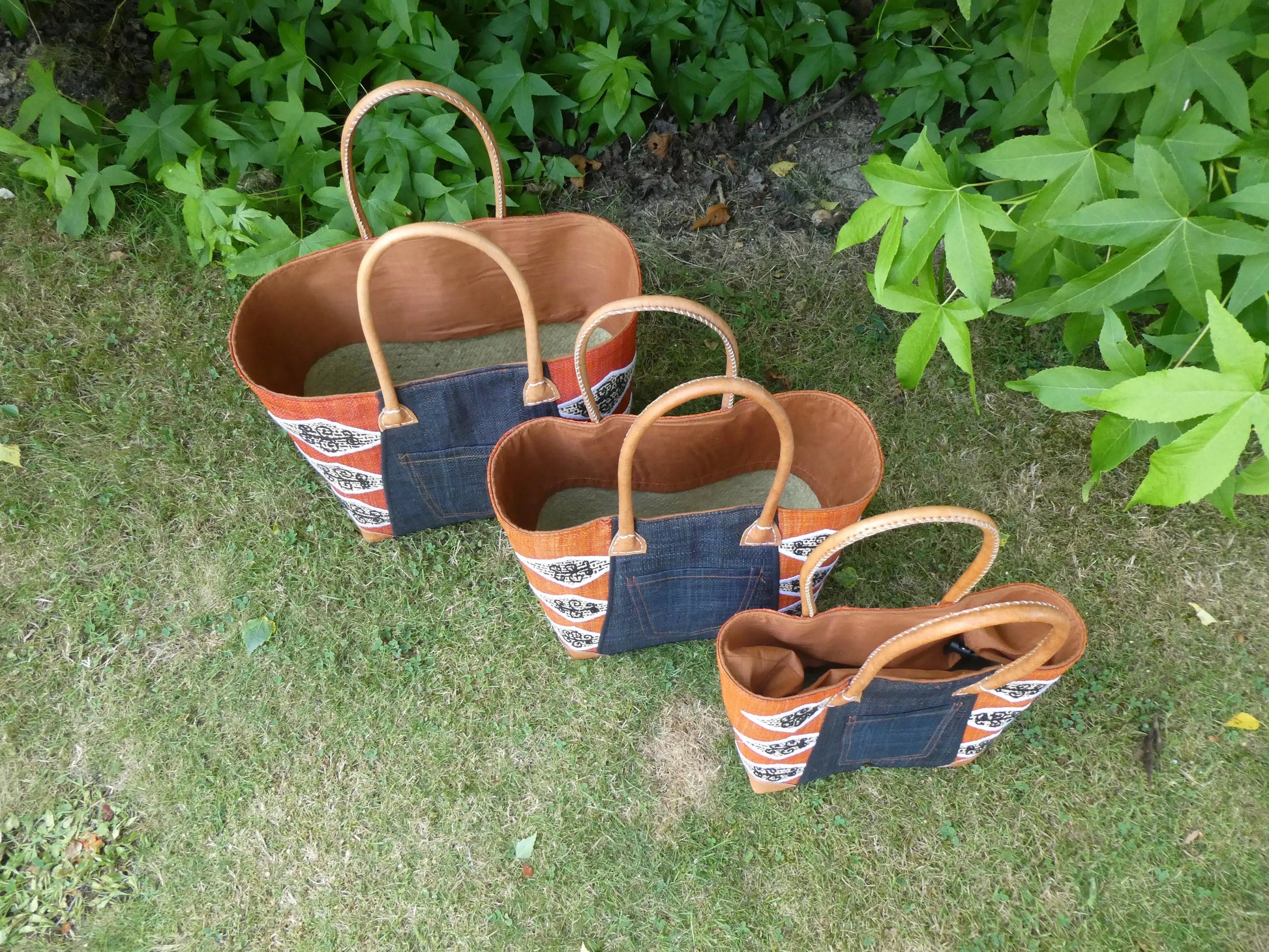 Cabas africain motif orange en cuir, panier artisanal trois tailles - vue du dessus des paniers sur herbe